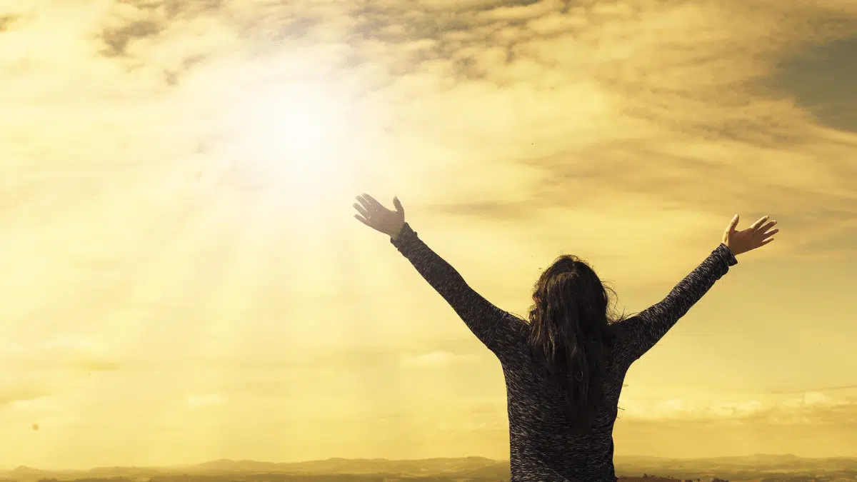 Shadow of a woman in front of a setting sun, arms lifted